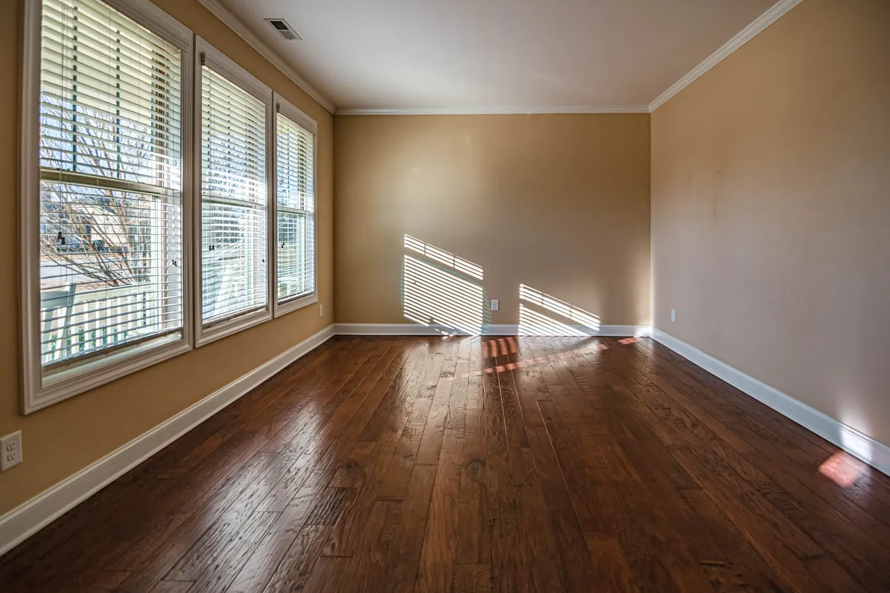 An empty rectangular room with a wooden floor, big windows and bare walls