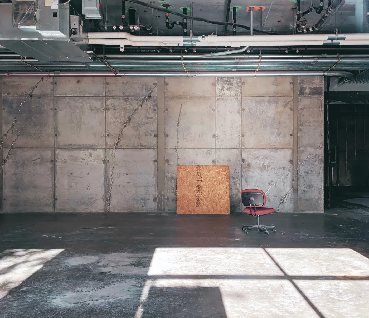 An echoey hall with concrete walls, a bare floor, a sheet of plywood and one chair