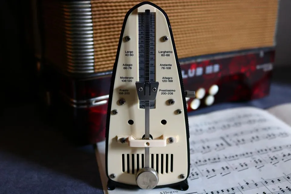 A traditional mechanical pendulum metronome with tempo markings on top of a music book