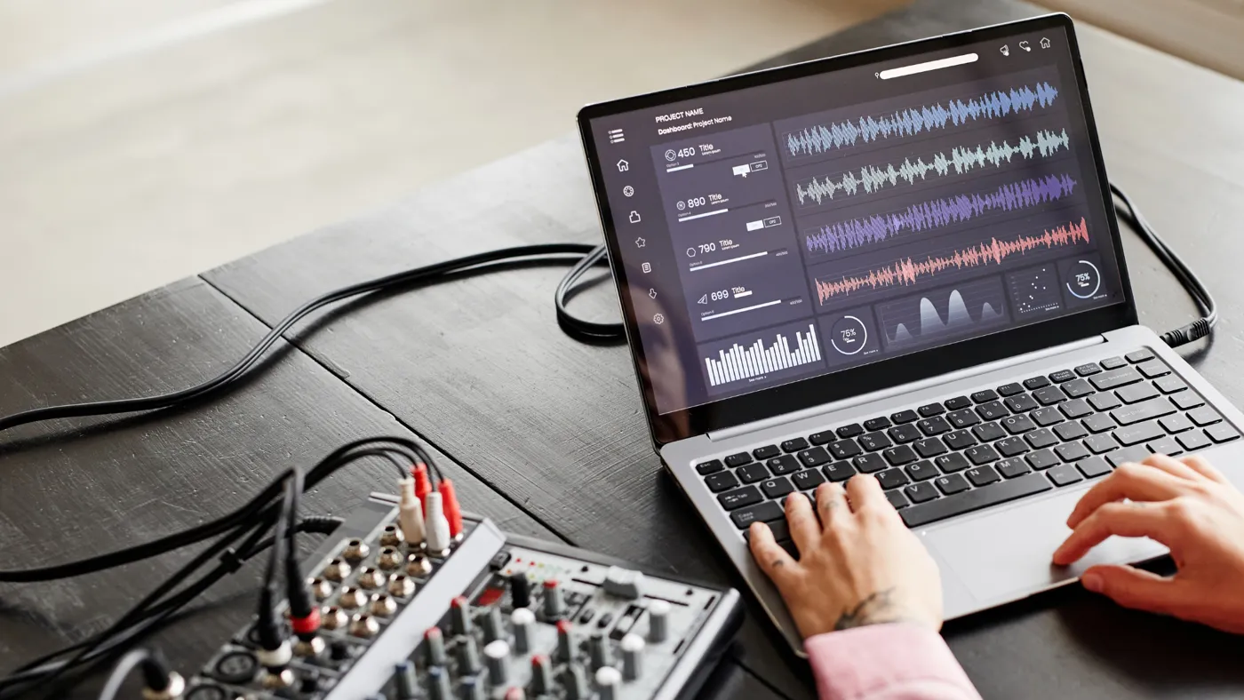 A mixer and a laptop with recorded audio tracks in a mixing program on the screen