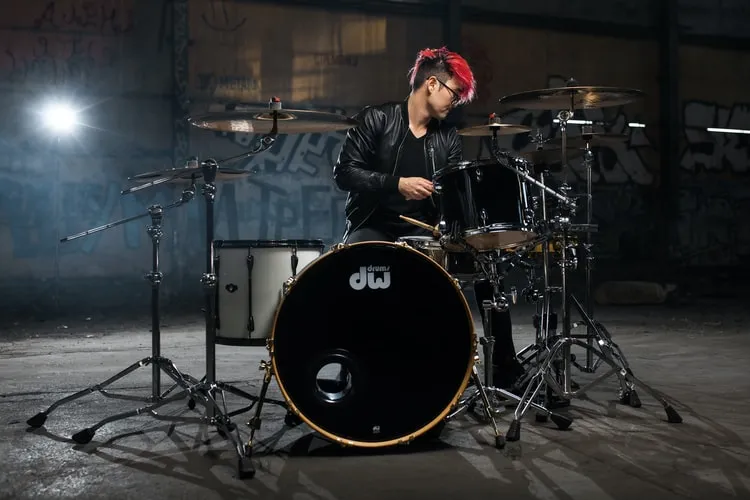 Comparison photo: drummer behind a dw kit in an empty hall, clean background with moody lighting