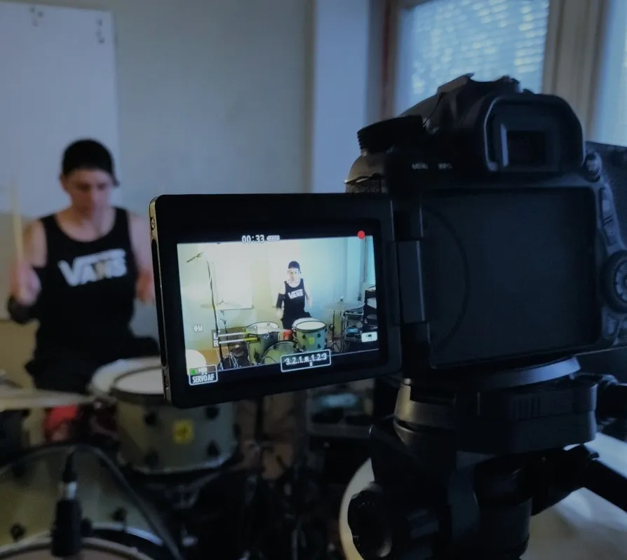 DSLR camera's flip screen on a tripod showing the drummer being filmed behind the kit