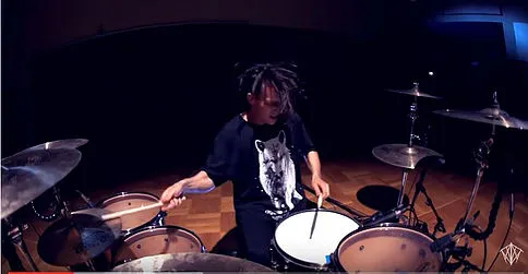 Drummer at a big kit, cymbals hung around them tilted slightly toward the player