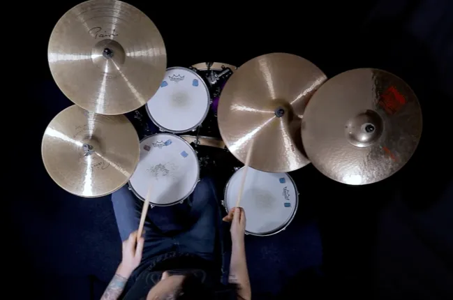 The same drum kit from above at another moment: the player's hands and sticks over the toms and snare