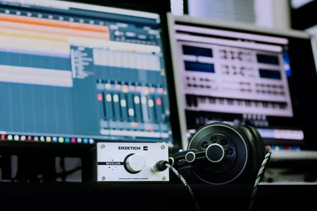 DAW on a computer screen with a headphone amp and headphones in front