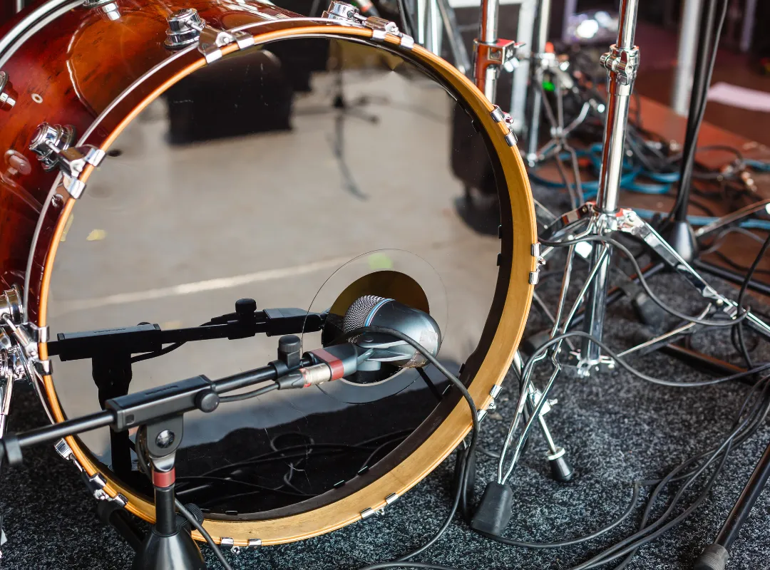 Microphone on a stand in front of the port hole in the bass drum's front head, with stands and cables in the background