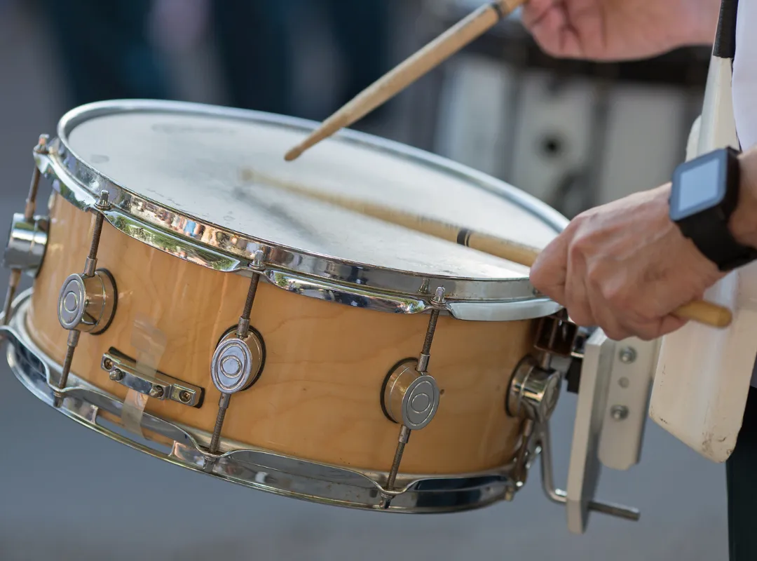 Drummer playing a wooden snare drum with sticks, close-up of the drumhead and tension rods