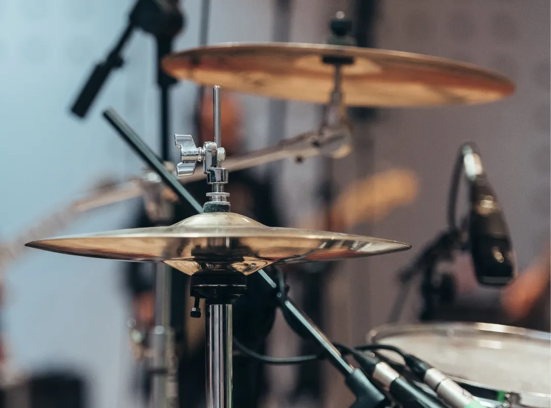 Close-up of a hi-hat and a crash cymbal on their stands, with microphones in the background
