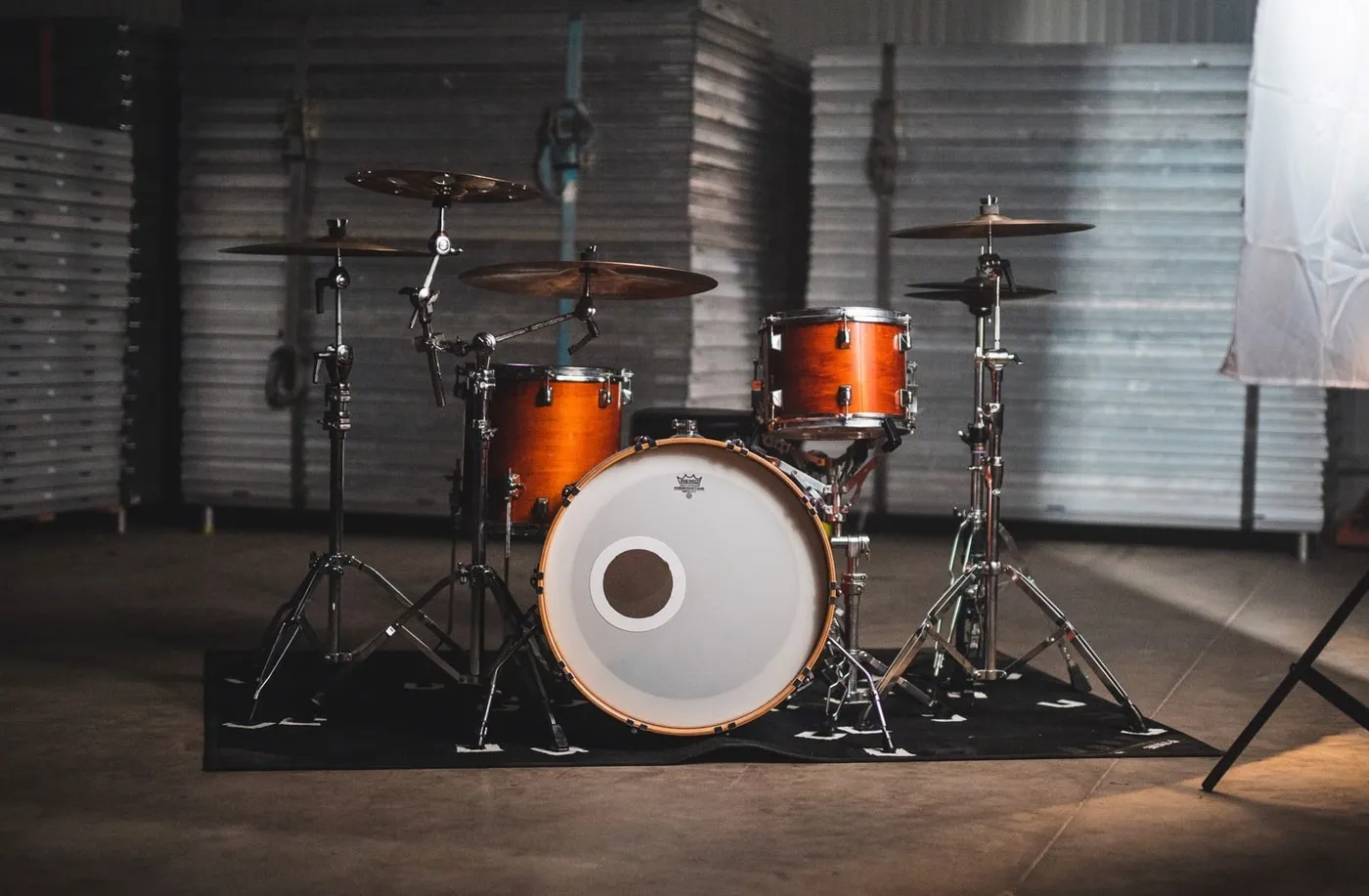 An orange acoustic drum kit with cymbals on a rug in a warehouse