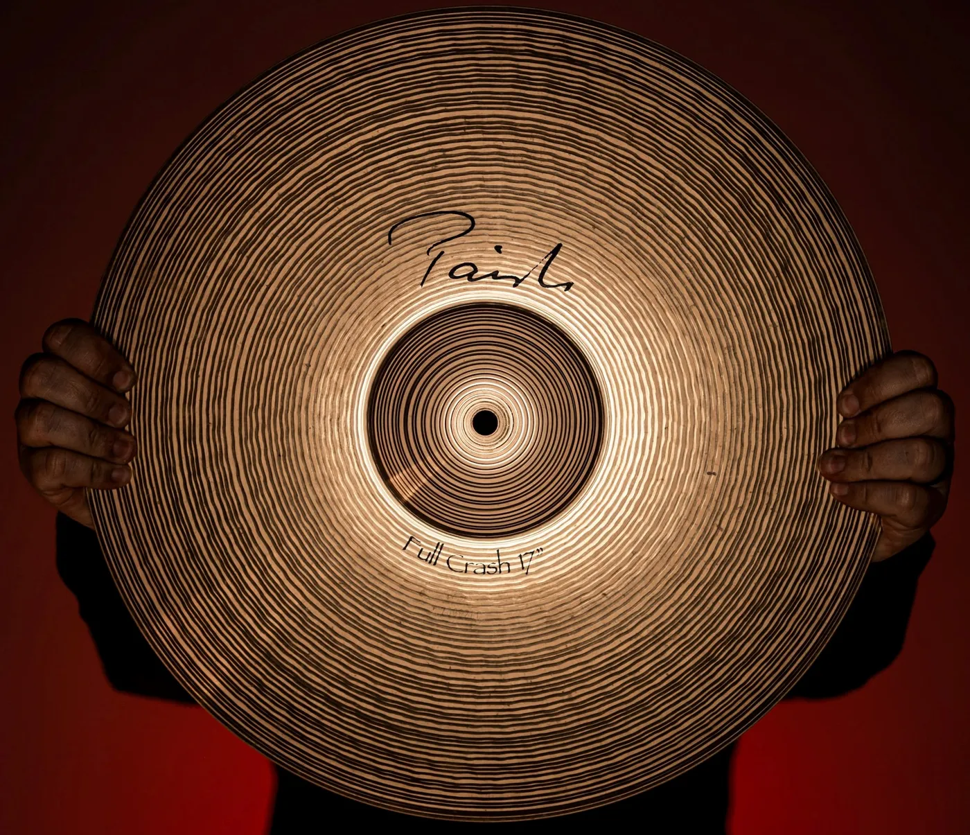 Hands holding a Paiste Signature Full Crash cymbal against the light