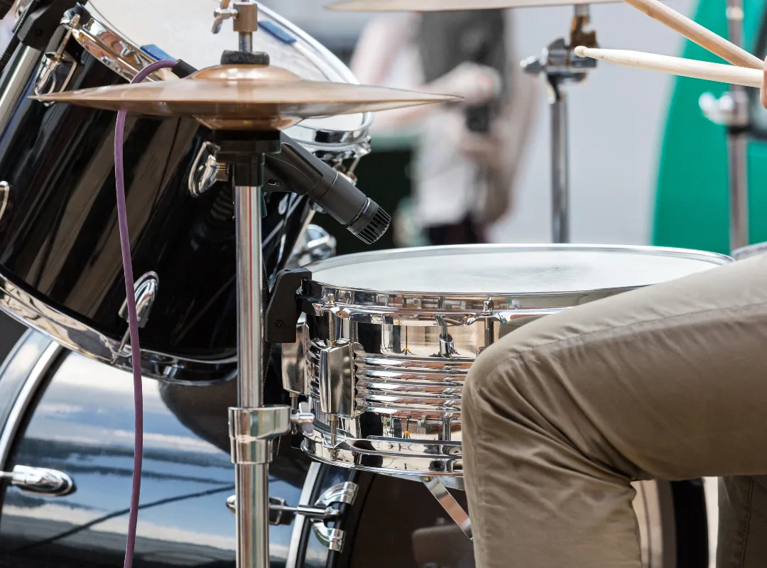 A hi-hat on its stand next to the snare, with a drummer playing with sticks