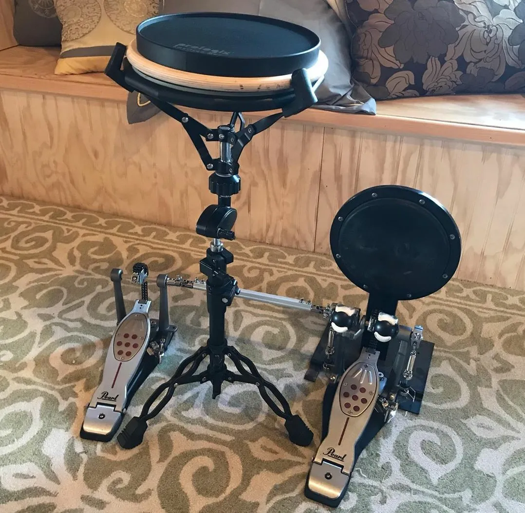 A drum pad on a snare stand, next to a practice pad with a double pedal