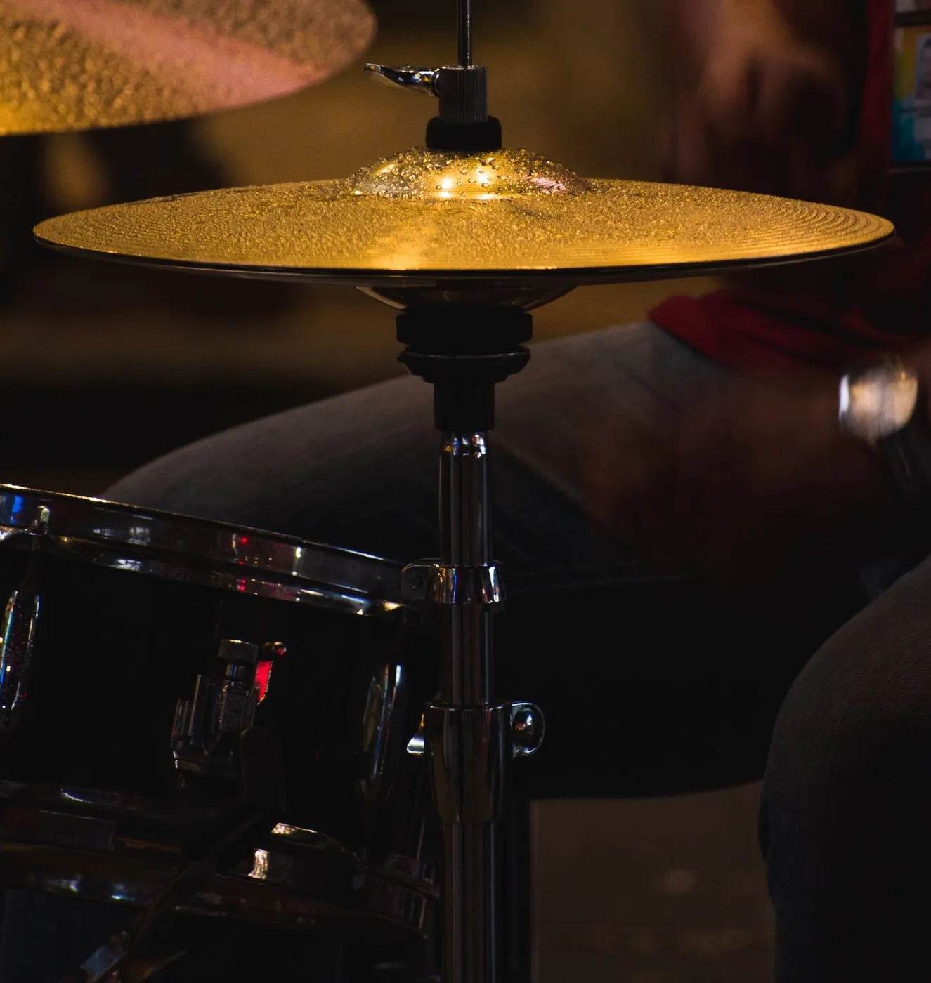Hi-hat cymbals on their stand next to the snare, with the drummer in the background
