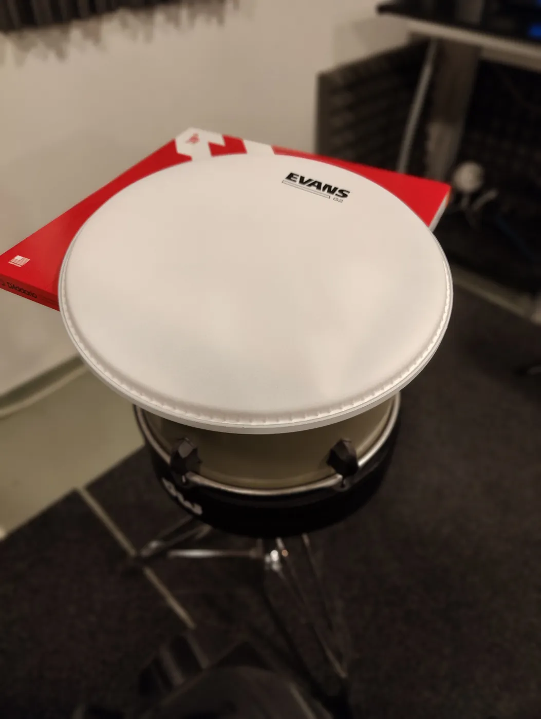 A new Evans drumhead on top of its package, with a tom on a drum throne underneath