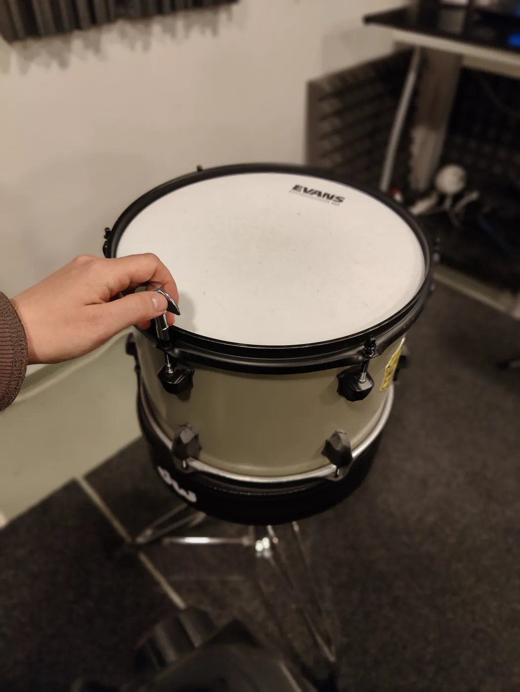 A hand loosening a tension rod on a tom