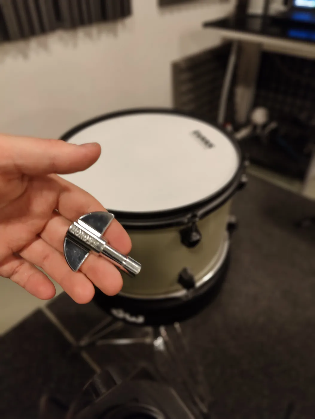 A drum key in hand, with the tom being tuned in the background