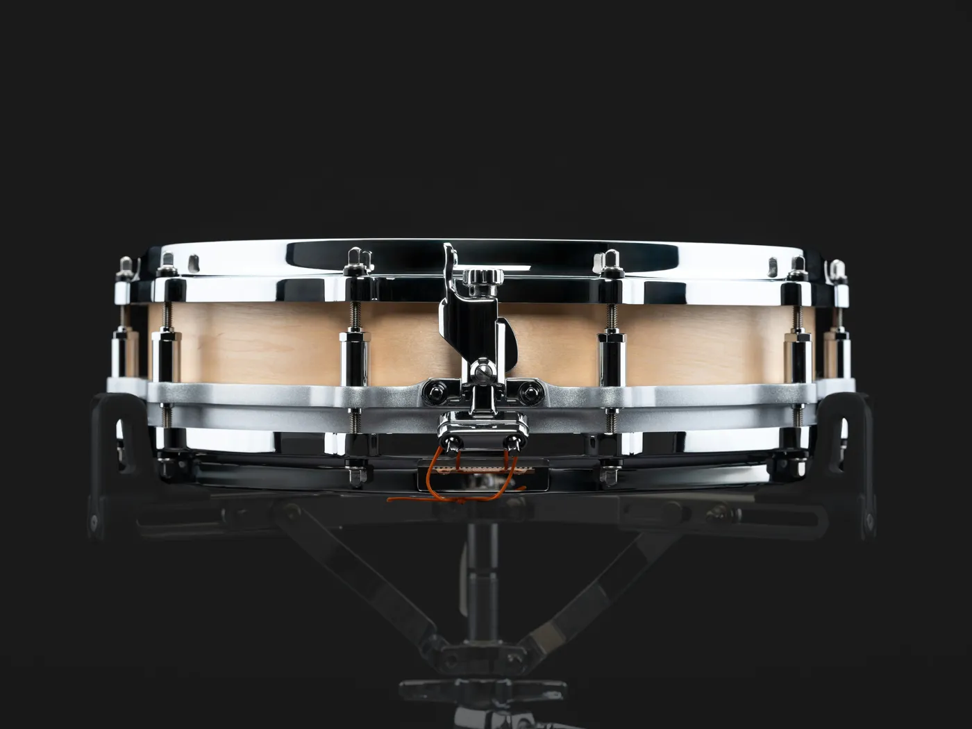 A shallow wood-shell piccolo snare on a stand, shot from the front
