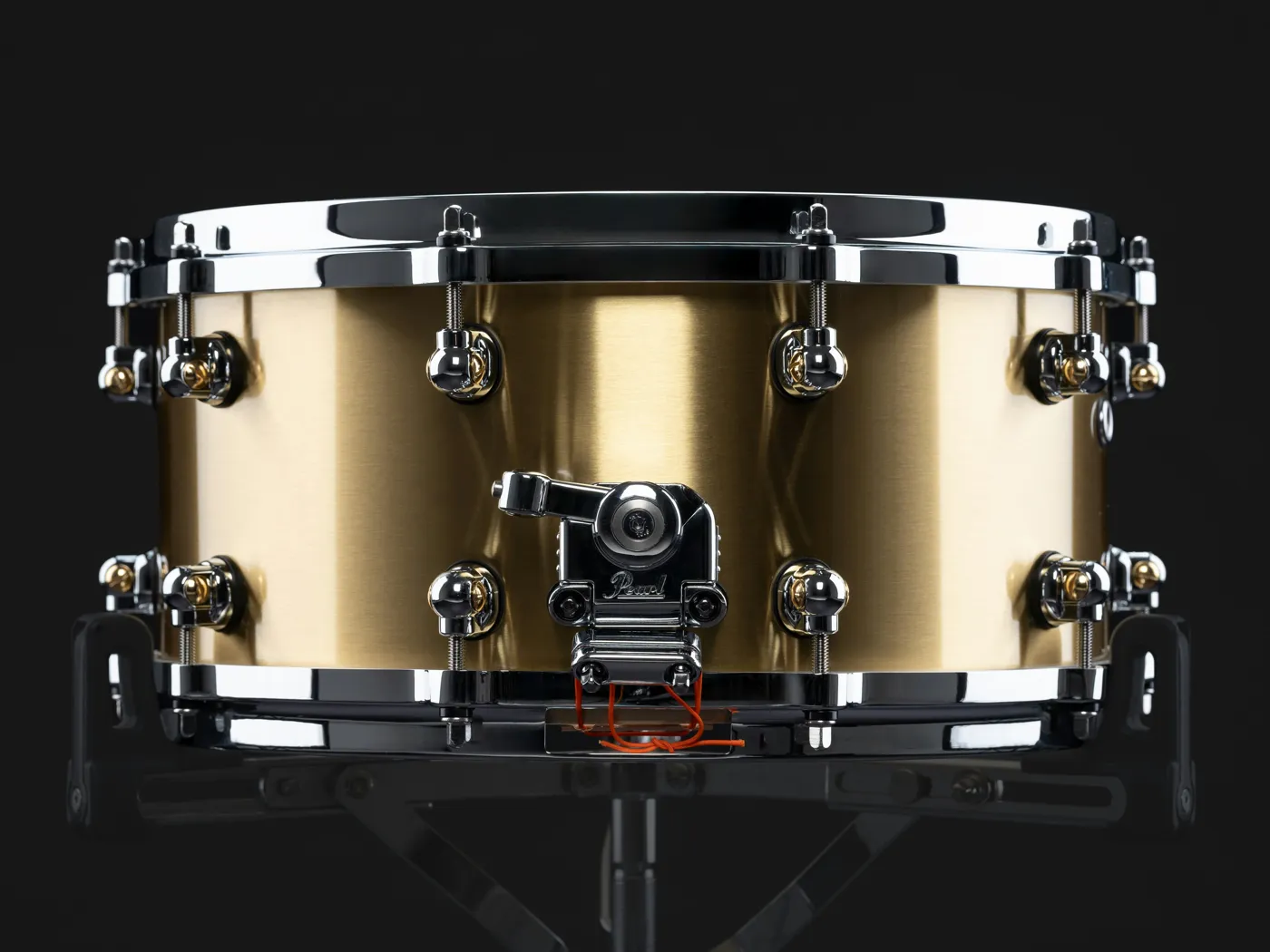 A brass-shell metal snare on a stand, with the snare strainer in front